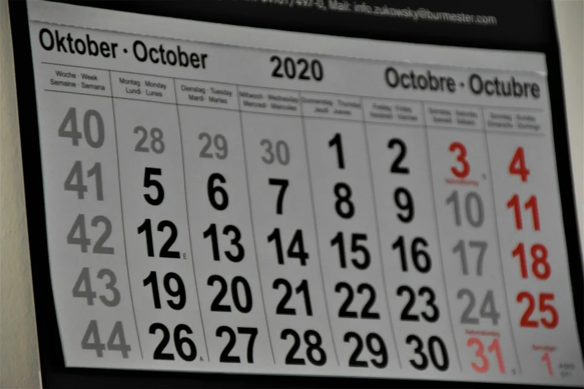 Calendrier mural annoté au crayon punaisé au-dessus d'un bureau