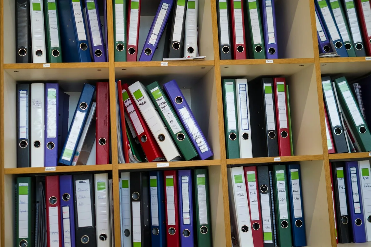 Classeur ouvert contenant des feuilles datées et des intercalaires posé sur une étagère