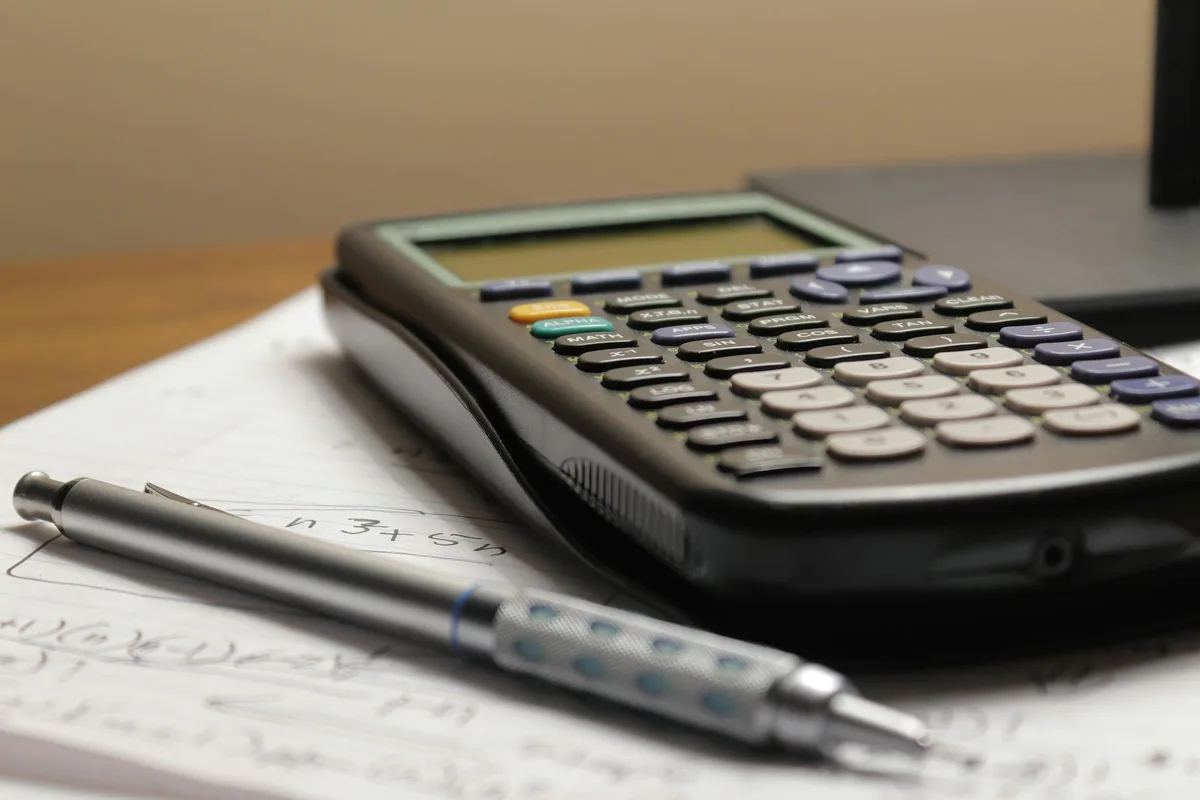 Calculatrice et stylo posés sur une feuille de calcul remplie à la main