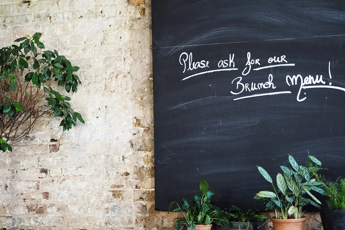 Ardoise de café portant une phrase courte écrite à la craie, posée contre un mur