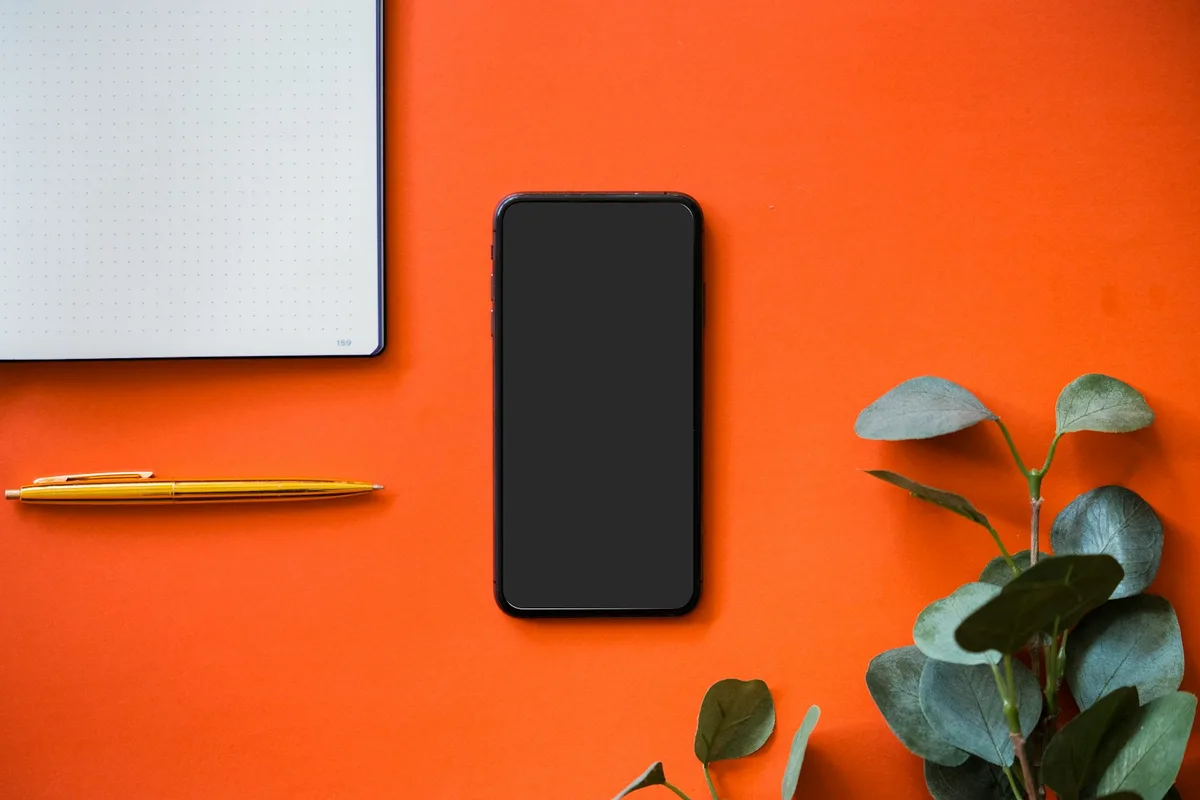 Téléphone affichant une liste de conversations posé près d'un carnet ouvert et d'un stylo