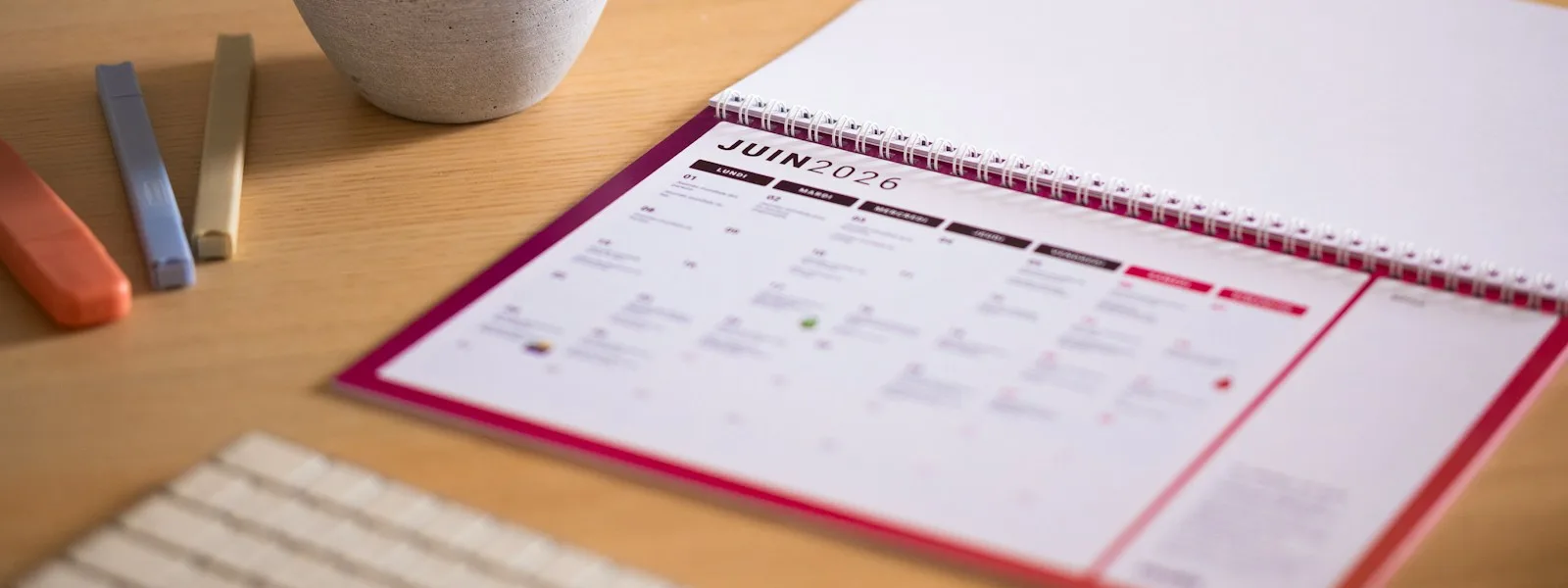 Agenda de bureau ouvert sur une page mensuelle, stylos et clavier posés à côté