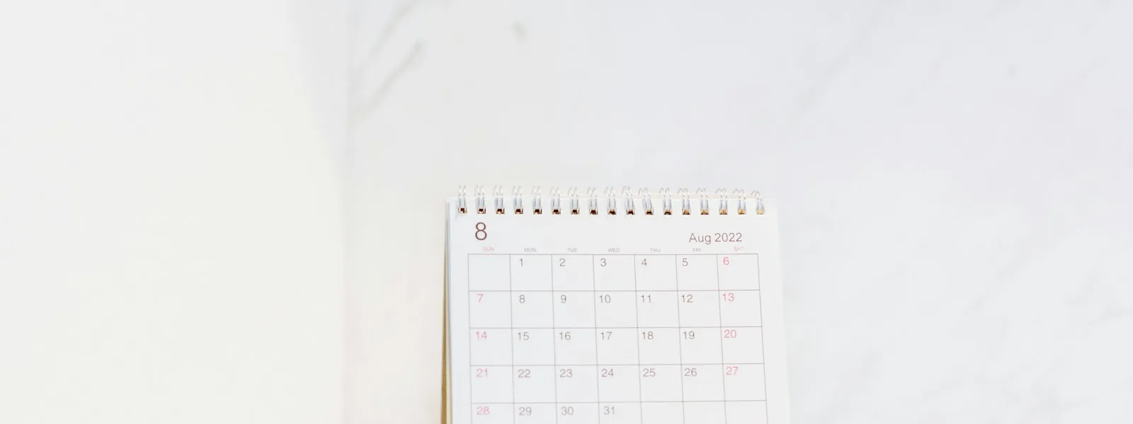 Un calendrier mensuel posé sur un bureau devant un écran, stylo à côté