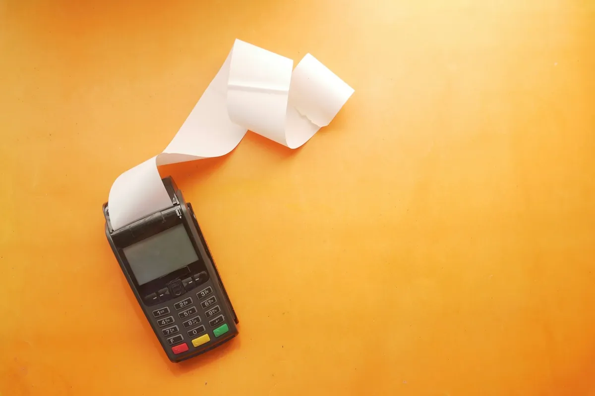 Un terminal de paiement et un long ticket déroulé sur fond orange