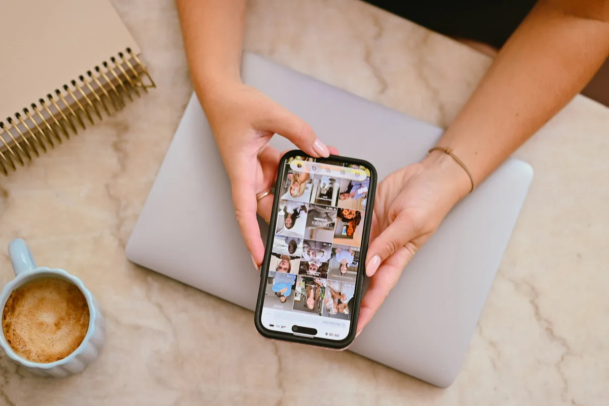 Deux mains tiennent un téléphone affichant un fil social au-dessus d'un ordinateur portable
