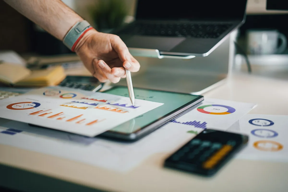 Une main désigne au stylet des graphiques imprimés posés près d'un ordinateur portable