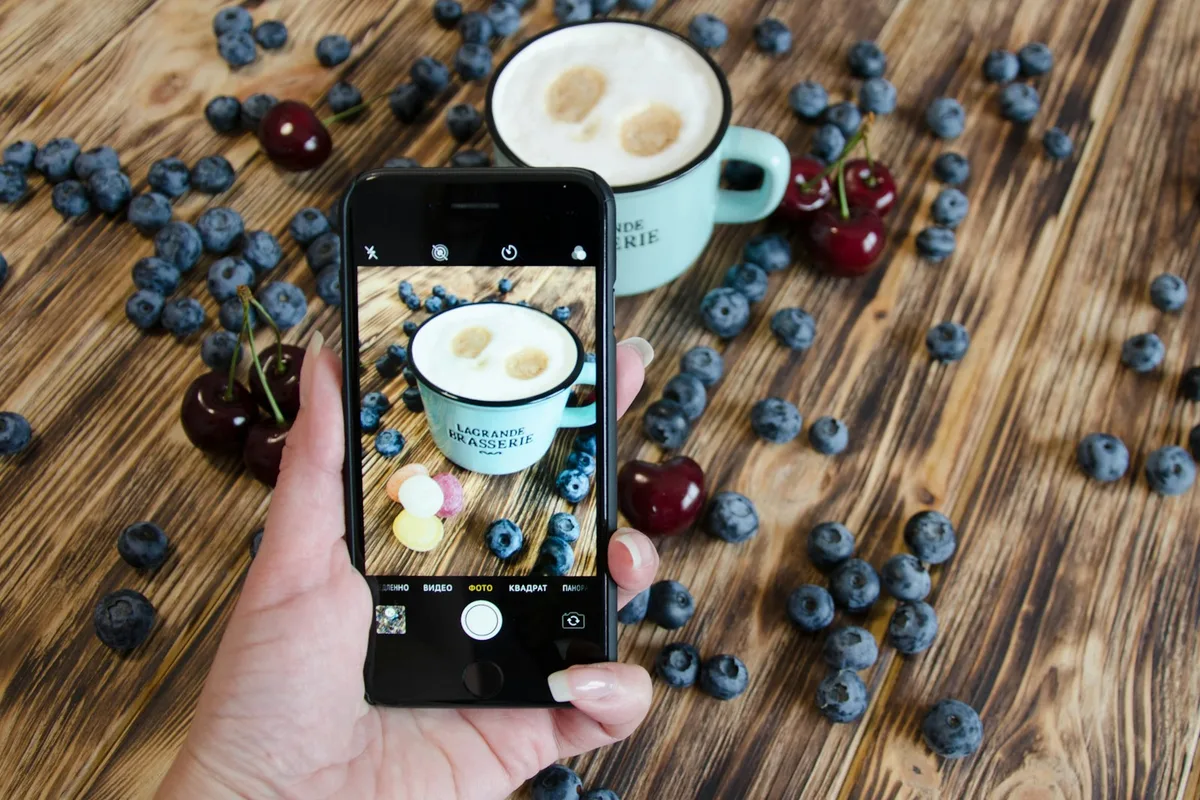Main photographiant un produit au téléphone sur une table en bois, en lumière naturelle