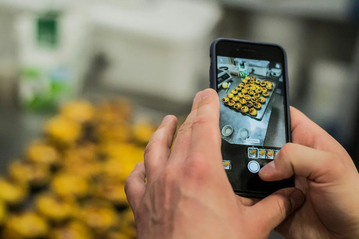 Deux mains photographient des produits posés sur un étal avec un téléphone