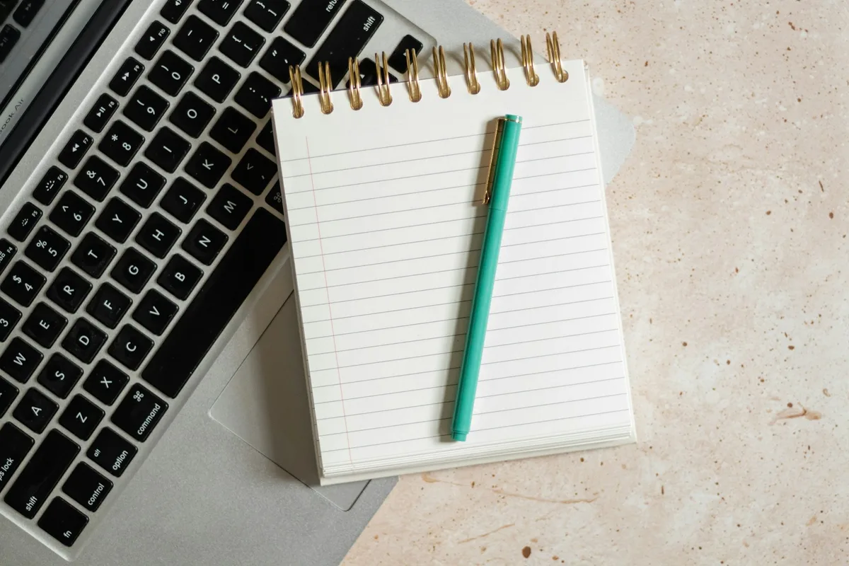 Un carnet et un stylo posés sur le clavier d'un ordinateur portable
