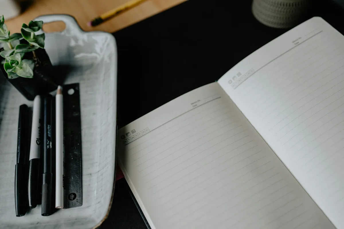 Cahier ouvert sur une page réglée et stylos posés dans un plateau