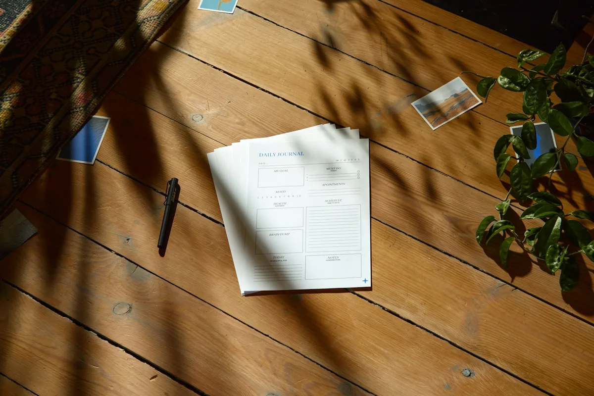 Deux feuilles imprimées et un stylo posés sur un plancher en bois
