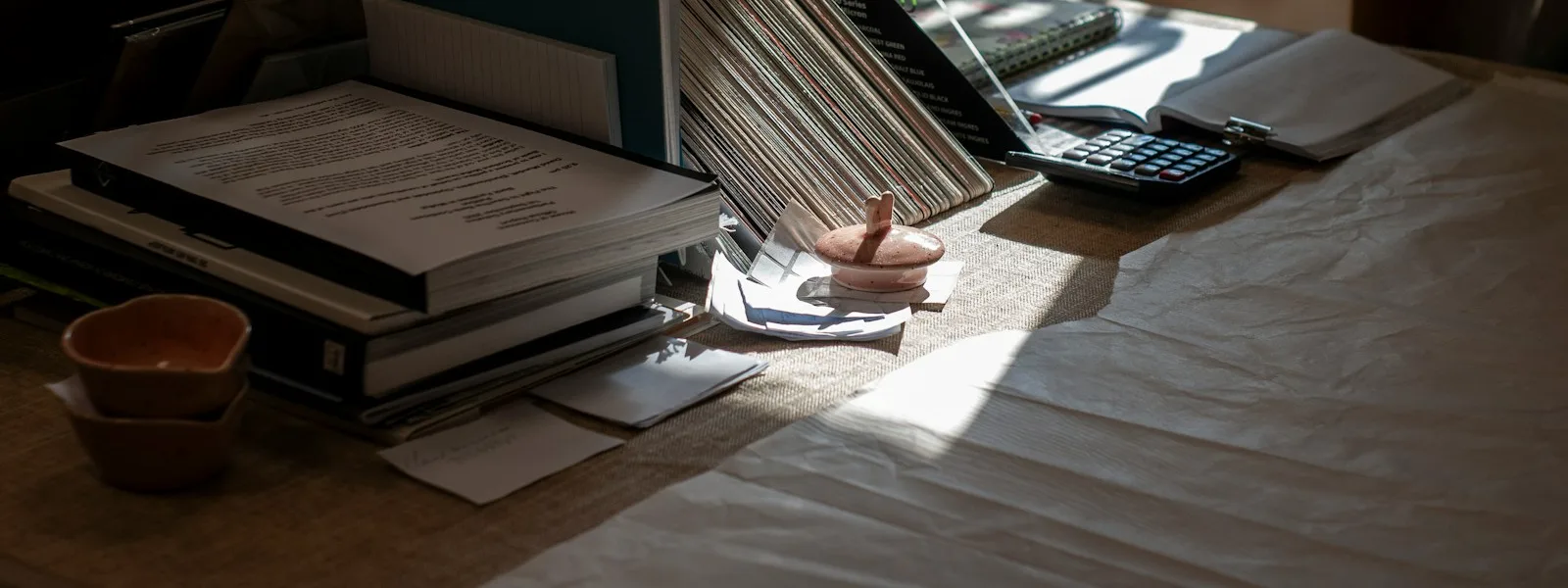Des dossiers, des papiers et une calculatrice empilés sur une table de bureau éclairée