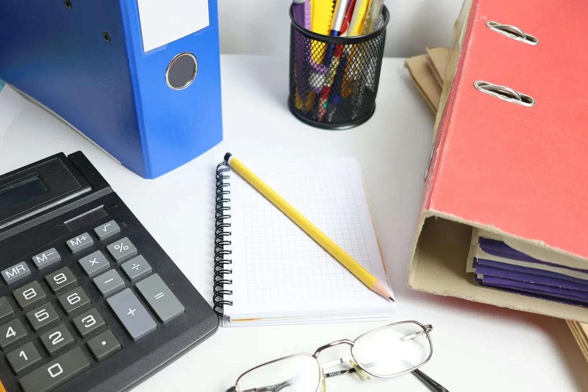 Des classeurs, une calculatrice et un carnet posés sur un bureau de comptabilité