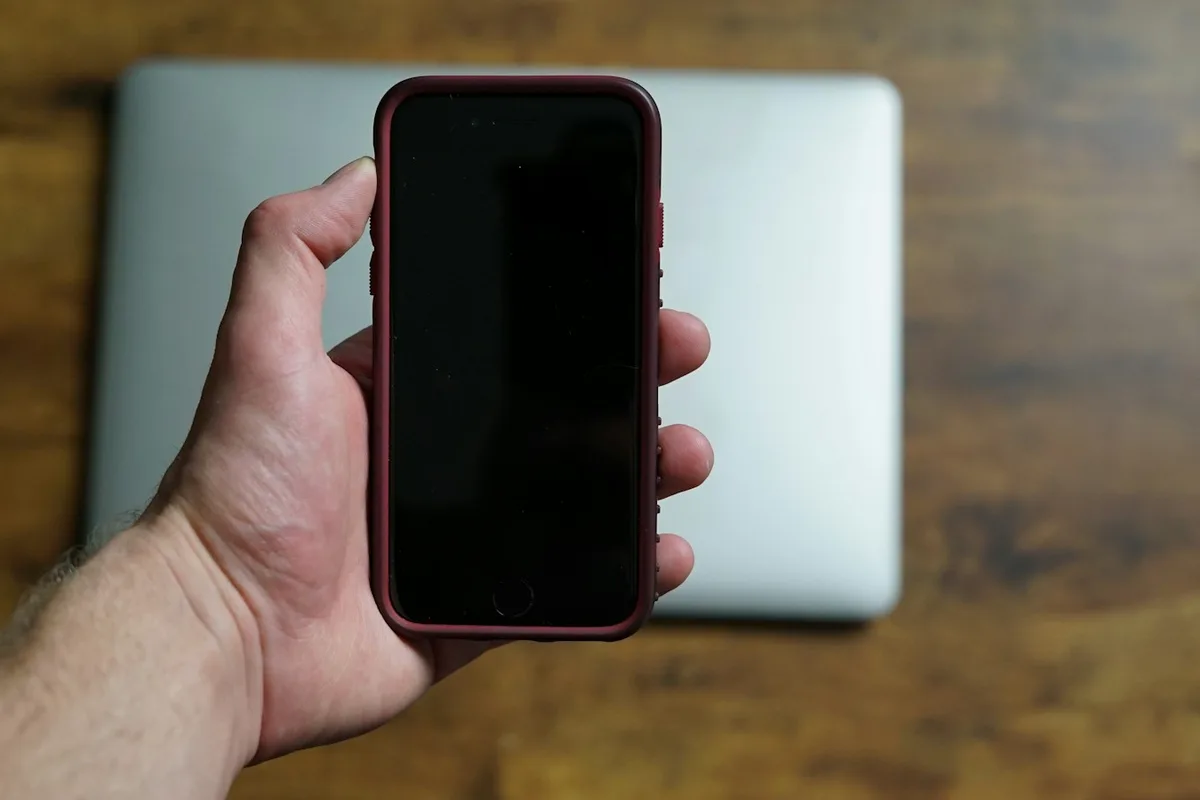 Une main tient un téléphone à écran éteint au-dessus d'un ordinateur portable fermé