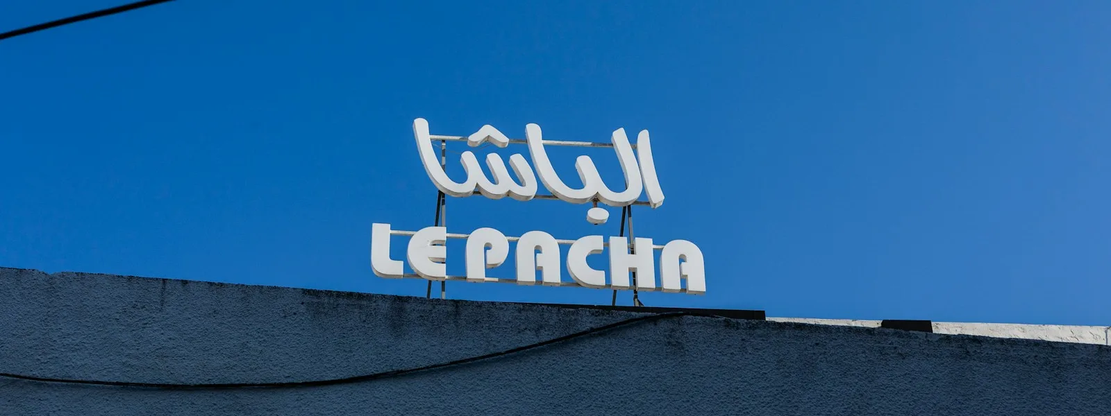 Enseigne bleue d'un commerce tunisien portant le même nom en arabe et en caractères latins