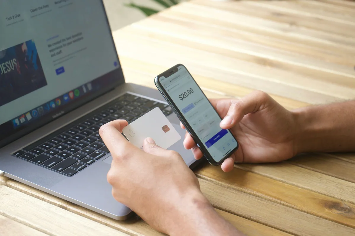 Une main tient une carte bancaire et un téléphone devant un écran de paiement