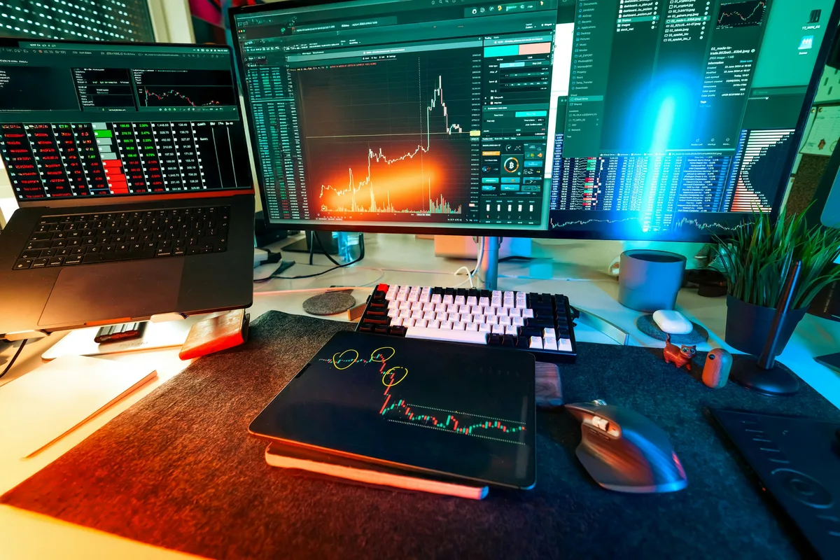 Plusieurs écrans affichent des courbes et des tableaux de suivi sur un bureau sombre