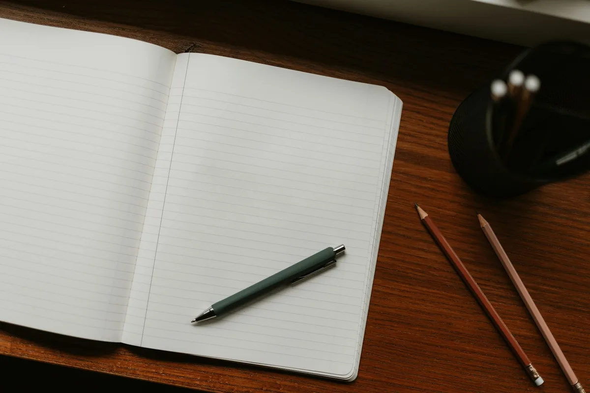 Un carnet ouvert avec un stylo et des crayons posés sur un bureau