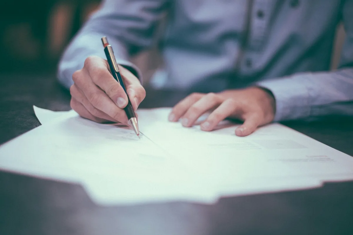 Deux mains remplissent au stylo un document imprimé posé sur une table sombre