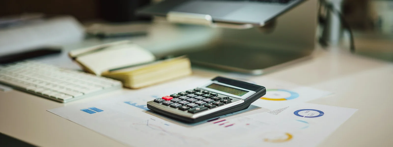 Une calculatrice, des graphiques imprimés et un clavier posés sur un bureau clair
