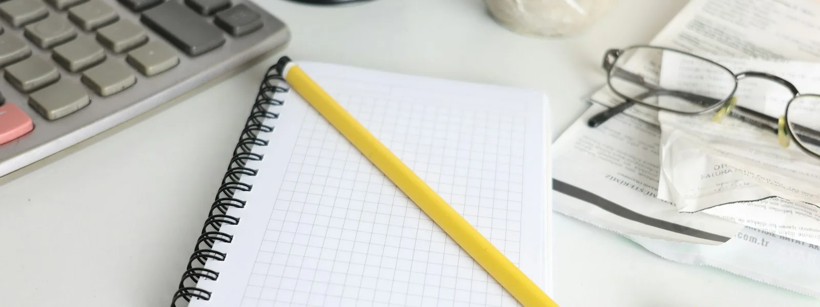 Calculatrice, bloc-notes, lunettes et factures posés sur un bureau de gestion