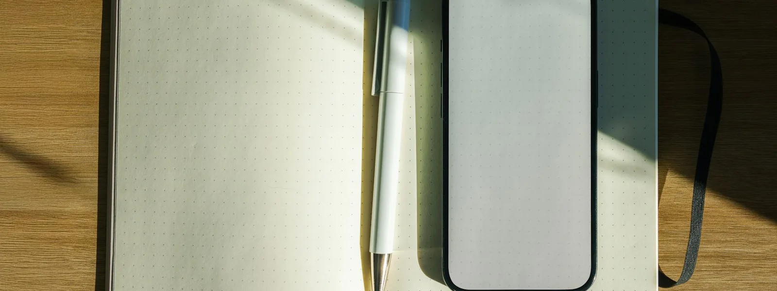 Un carnet ouvert, un stylo et un téléphone posés sur un bureau en bois ensoleillé