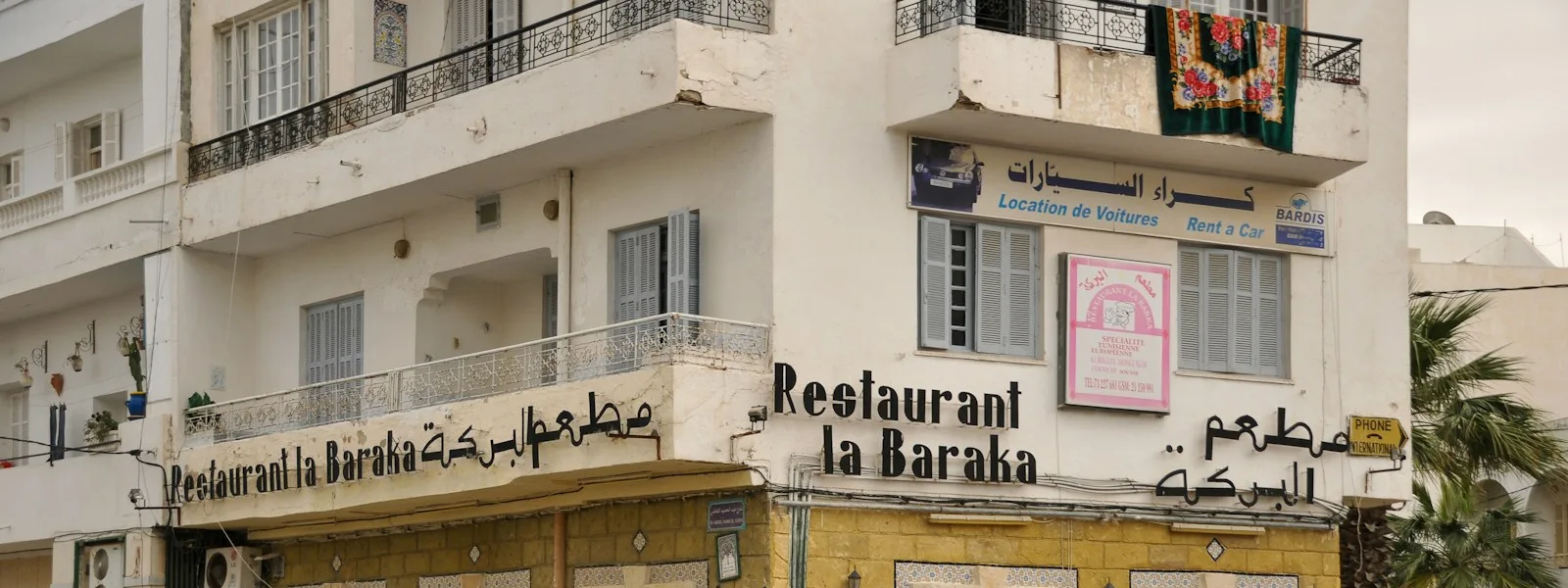 Façade d'un restaurant tunisien à l'angle d'une rue, enseigne bilingue et voitures garées