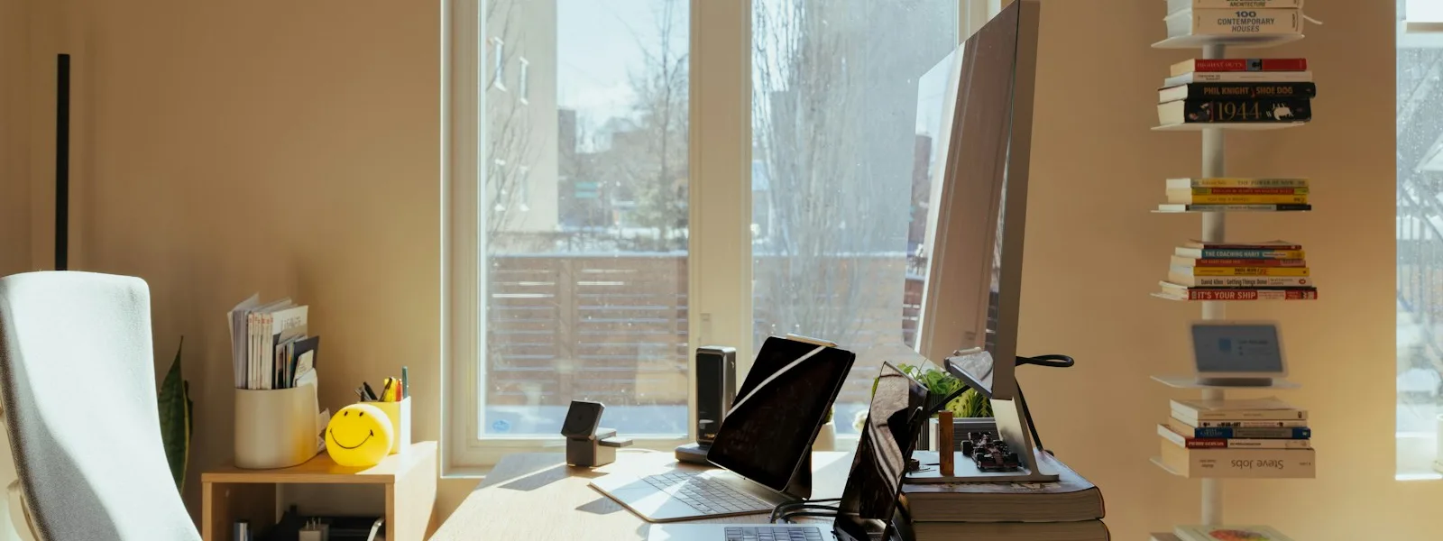 Bureau baigné de lumière avec écran, clavier et étagère de livres près d'une fenêtre
