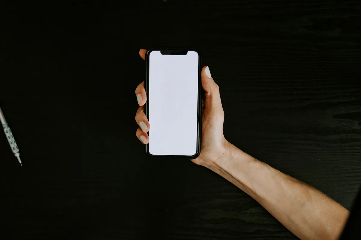 Une main tient un téléphone à l'écran vide, sur fond sombre
