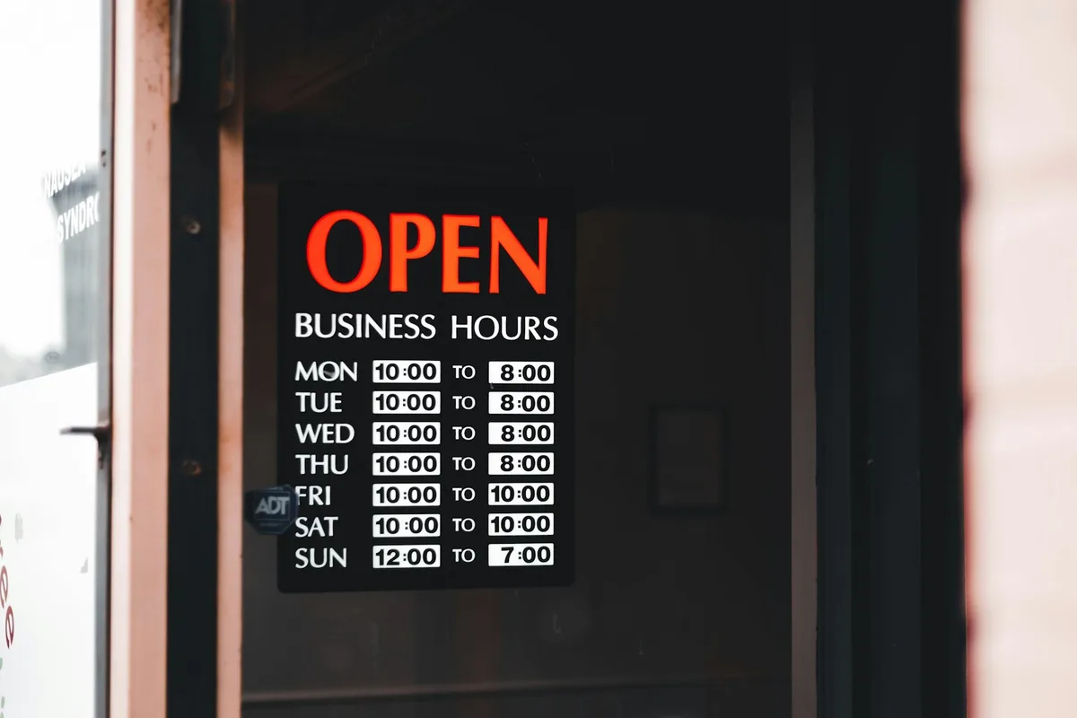 Un panneau d'horaires d'ouverture affiché sur la porte vitrée d'un commerce