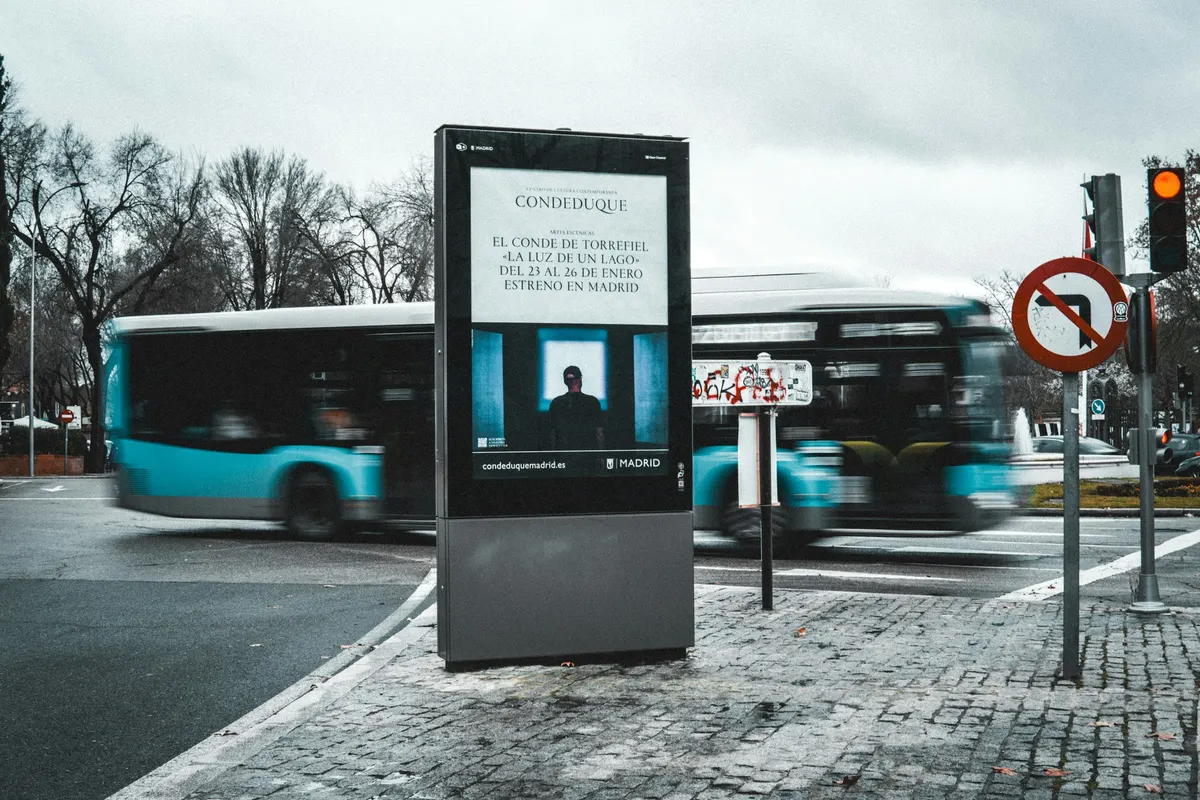Un panneau publicitaire numérique éclairé en bord de rue, un bus passe devant