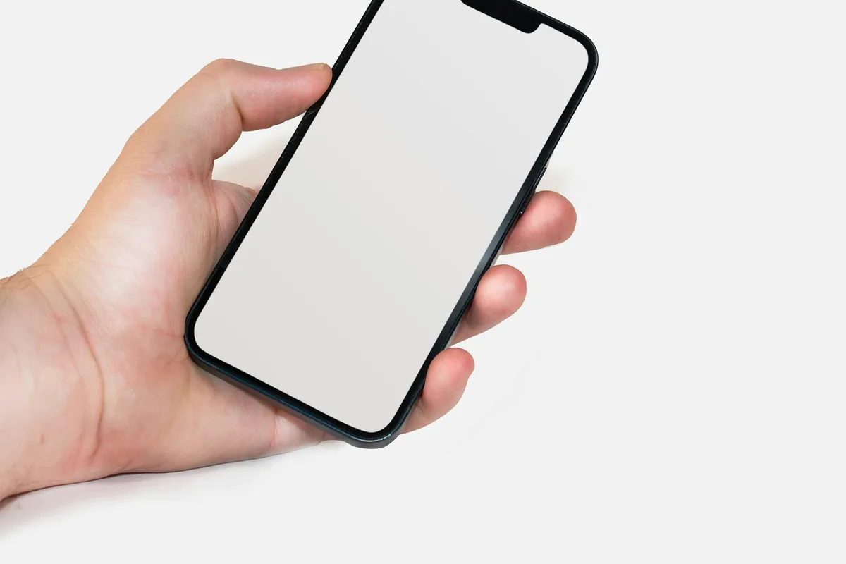 Une main tient un téléphone à l'écran vierge devant un fond sombre