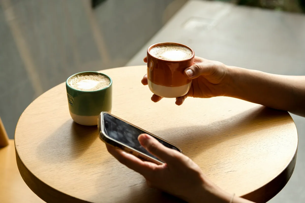 Une main tient un téléphone allumé à côté d'un café sur une table ronde
