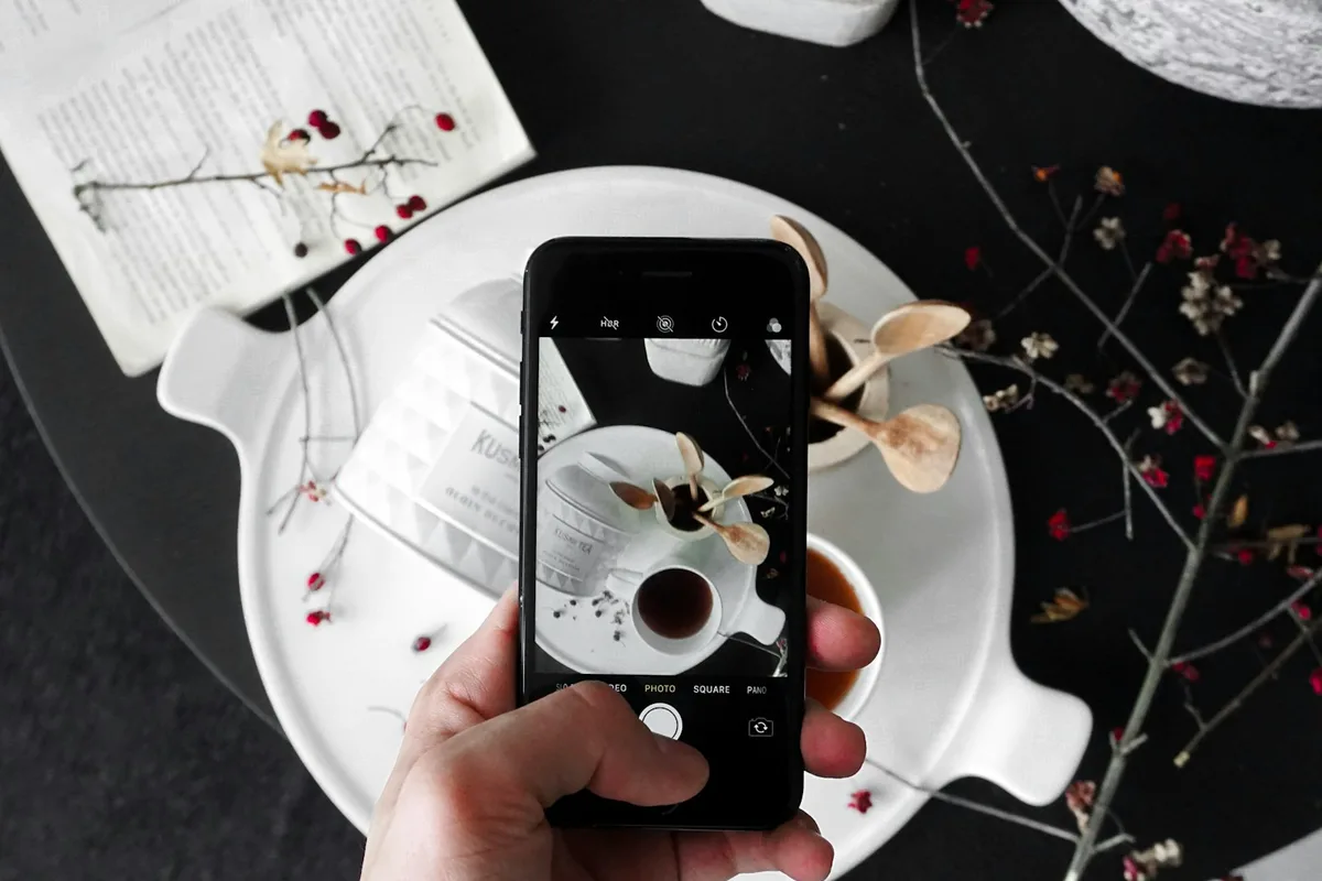 Une main photographie au téléphone une tasse posée sur un plateau blanc