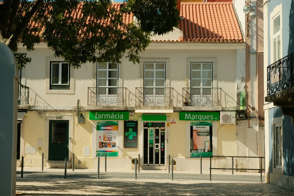 Croix verte de pharmacie fixée en façade, vue de trois quarts contre le ciel