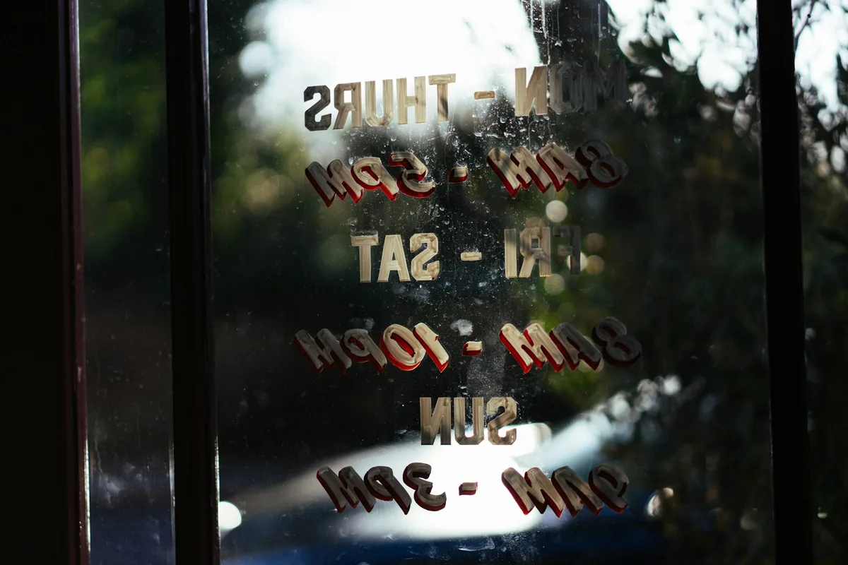 Écriteau d'horaires d'ouverture accroché derrière une porte vitrée donnant sur la rue