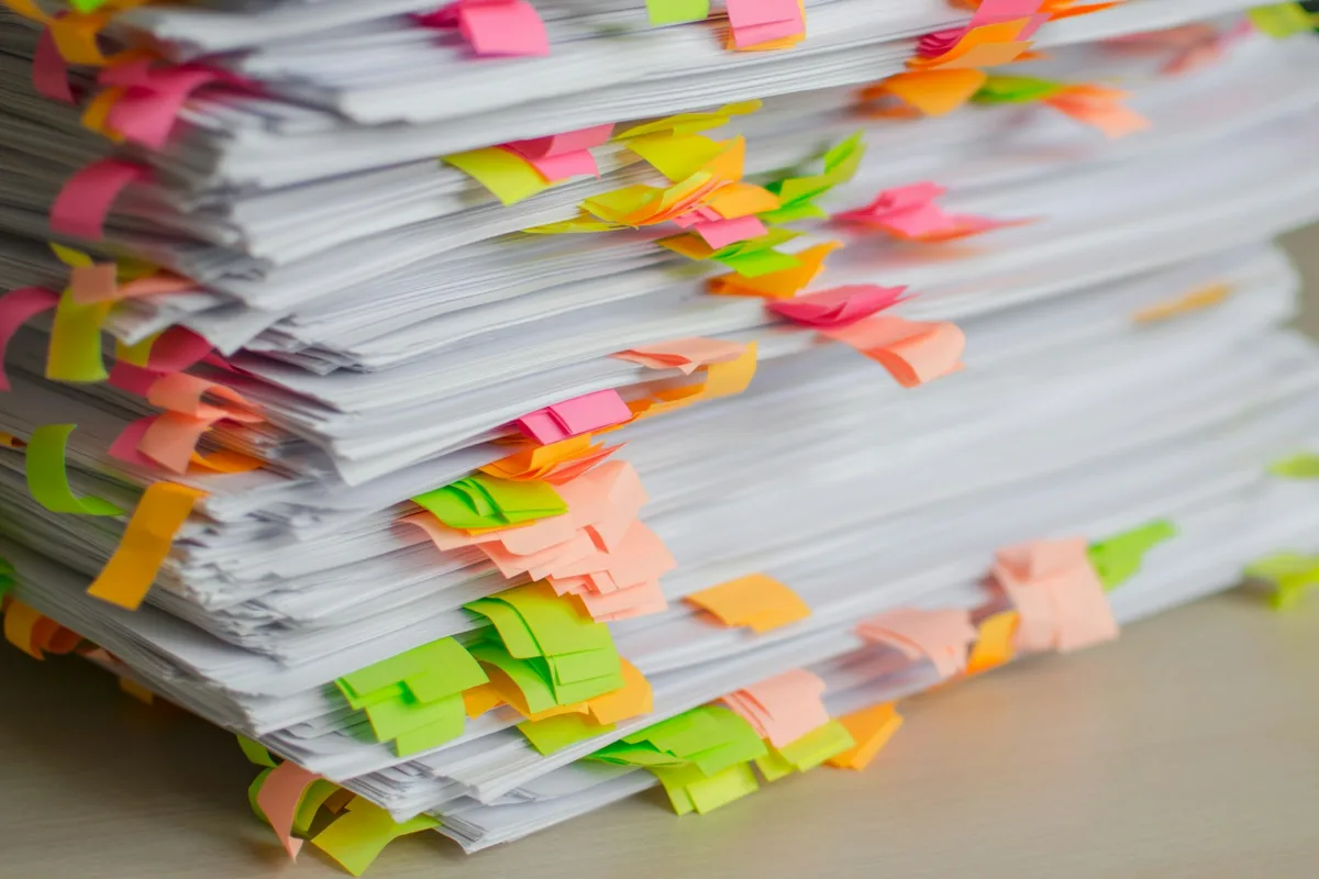 Pile de documents imprimés hérissée d'onglets adhésifs de couleur posée sur un bureau