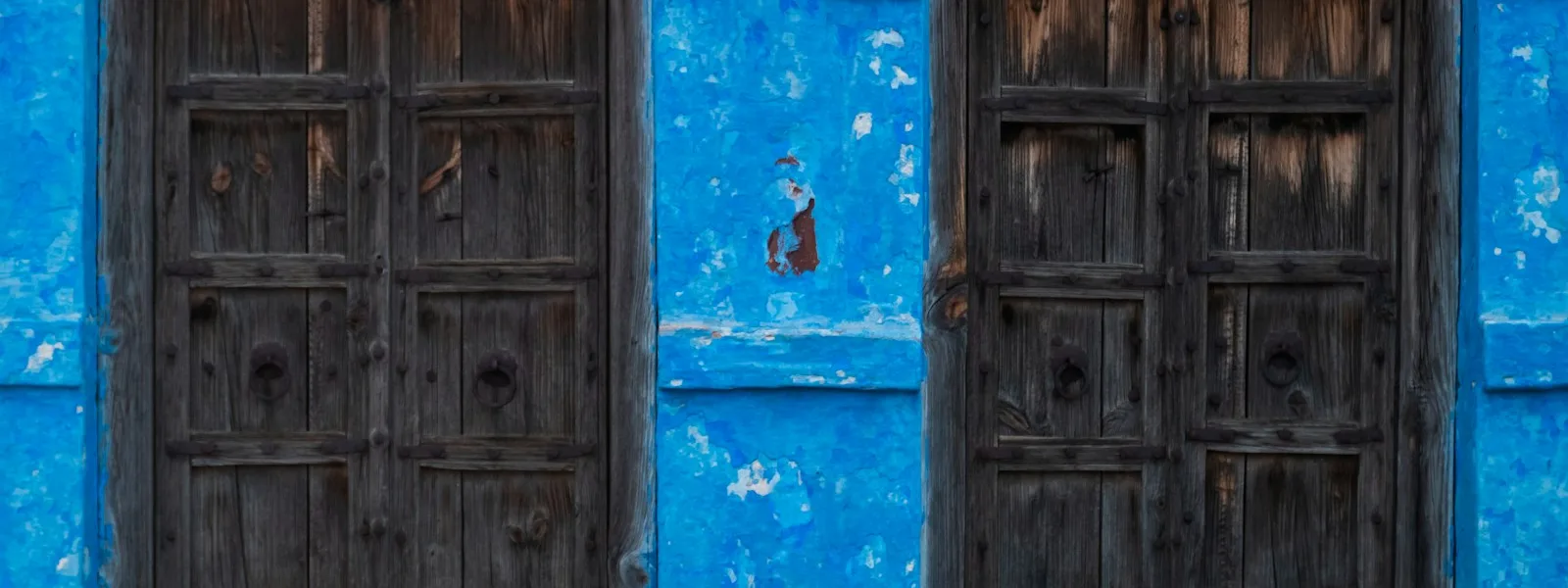 Deux portes en bois anciennes côte à côte dans un mur bleu écaillé