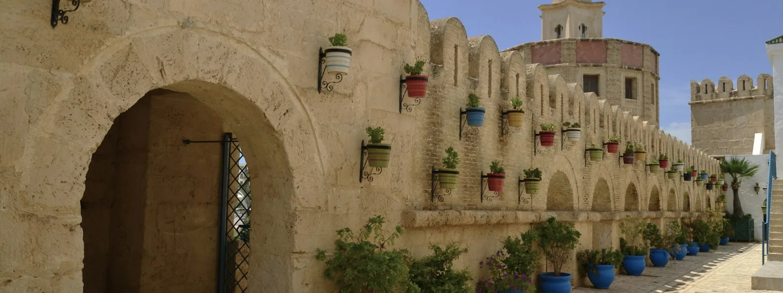 Ruelle d'une médina tunisienne bordée d'arcades et de pots de fleurs bleus