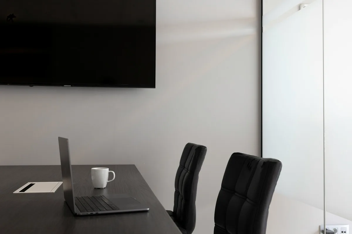 Table de réunion avec un ordinateur portable ouvert, une tasse et deux chaises vides