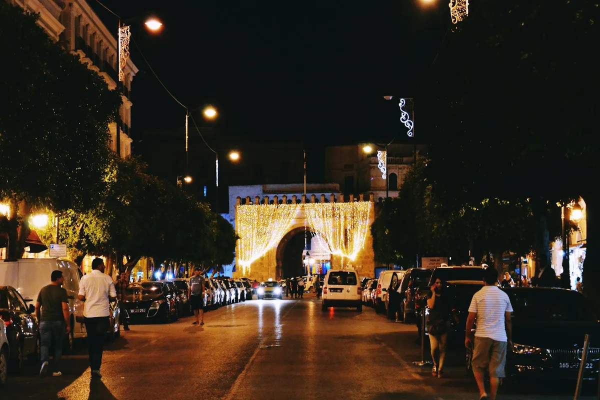 Avenue commerçante de Tunis éclairée en soirée, passants et devantures ouvertes près de la médina