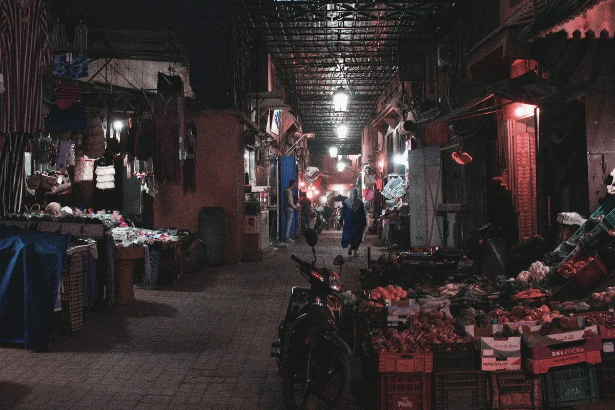 Ruelle marchande éclairée en soirée, étals et vitrines ouverts sous les lumières