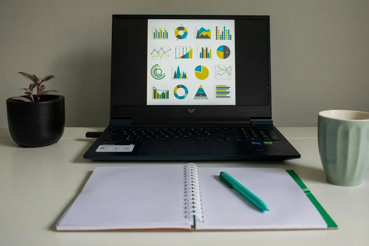 Un ordinateur portable affiche des graphiques de répartition à côté d'un carnet ouvert