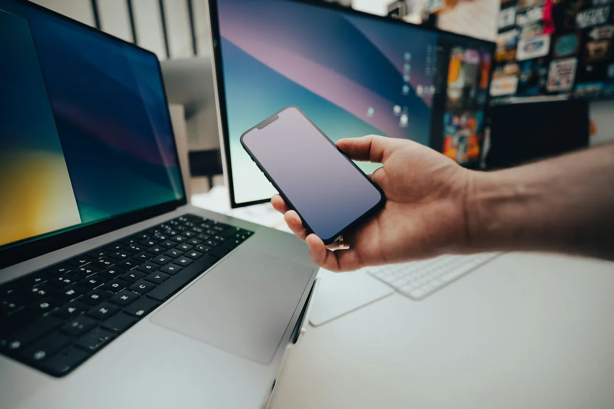 Une main tient un téléphone à côté d'un ordinateur portable ouvert sur un bureau