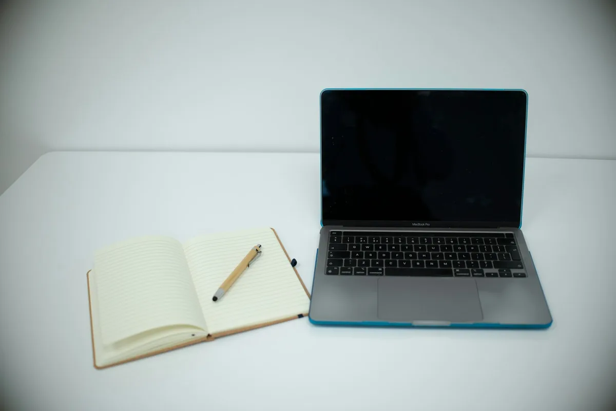 Un carnet ouvert et un stylo posés à côté d'un ordinateur portable