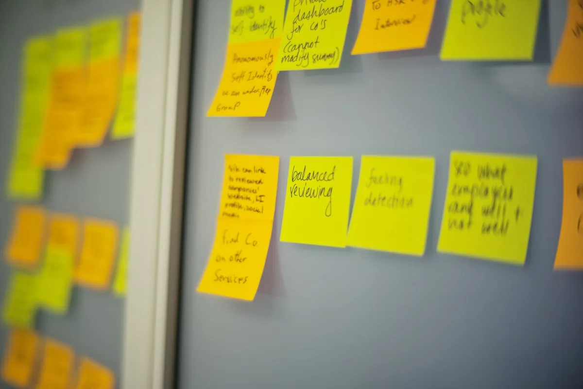 Des notes autocollantes jaunes et orange alignées en rangées sur un mur clair